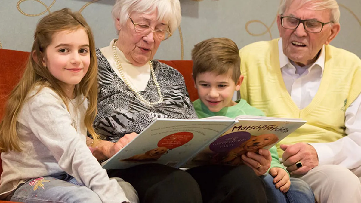 Ehepaar, das im PFLEGEN & WOHNEN HAMBURG Finkenau lebt, liest seinen Enkelkindern vor.