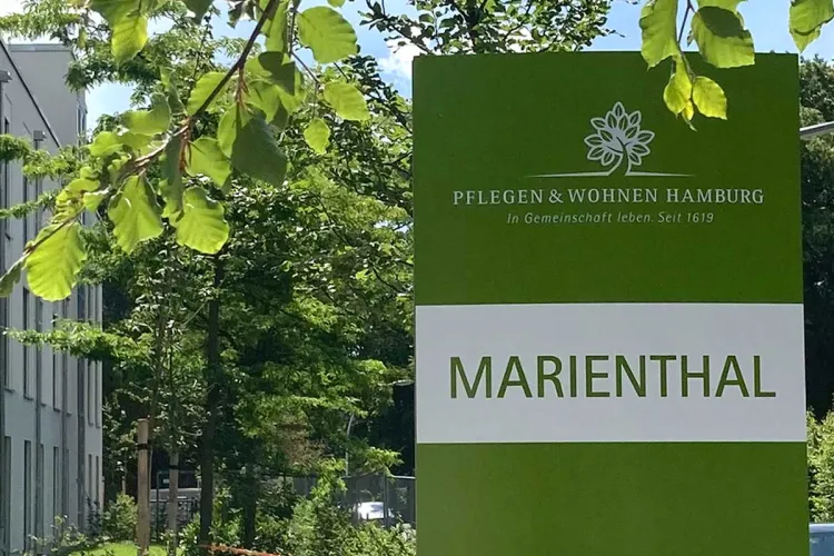 Grünes Schild mit Logo und Schriftzug von PFLEGEN & WOHNEN HAMBURG am Standort Marienthal.