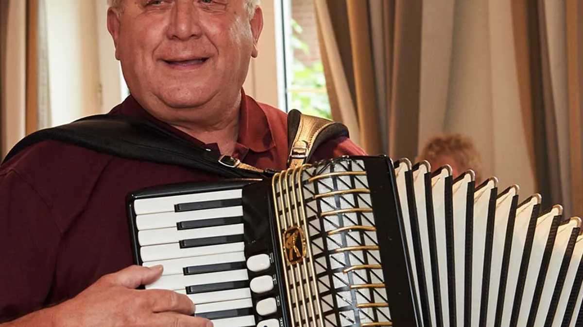 Bewohner von PFLEGEN & WOHNEN HAMBURG in Horn spielt lächelnd Akkordeon als Freitzeitaktivität.