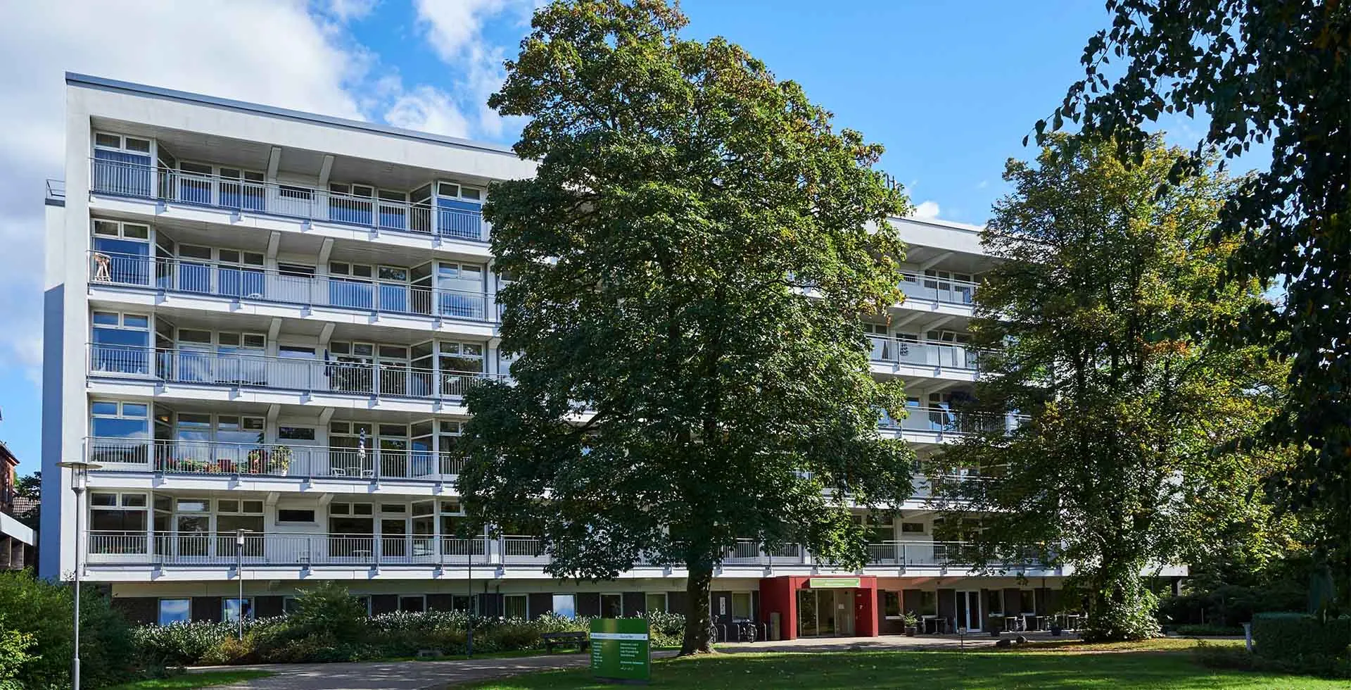 Außenansicht: PFLEGEN & WOHNEN HAMBURG Horn am Husarendenkmal mit Bäumen und Grünflächen für pflegebedürftige Senioren.