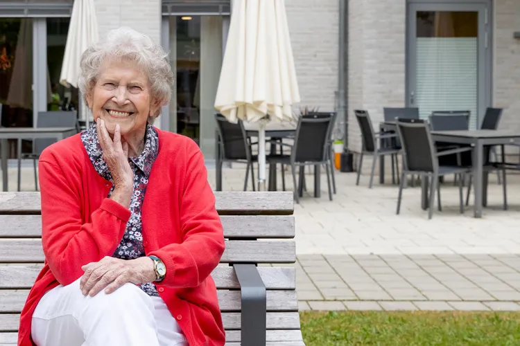 Auf einer Bank sitzt strahlend die Bewohnerin von PFLEGEN & WOHNEN MARIENTHAL, Inge Rilk.
