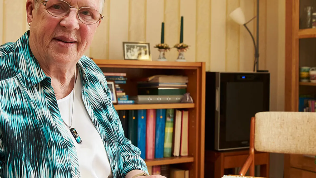 Bewohnerin sitzt am Tisch in ihrem gemütlich eingerichteten Zimmer im PFLEGEN & WOHNEN HAMBURG Finkenau.